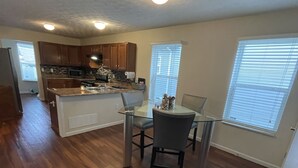 A spacious kitchen with wooden cabinets, a central island, and a dining area with a glass table and chairs. - Central Columbus Home sure to fit all of your needs. (Columbus)