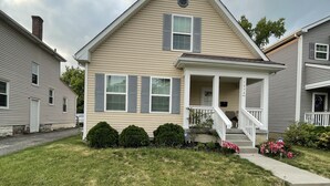 A two-story house with a front porch, a chimney, and a small front yard with grass and shrubs. - Central Columbus Home sure to fit all of your needs. (Columbus)
