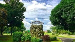 A golf course entrance with a stone sign, lush greenery, and a curved road.