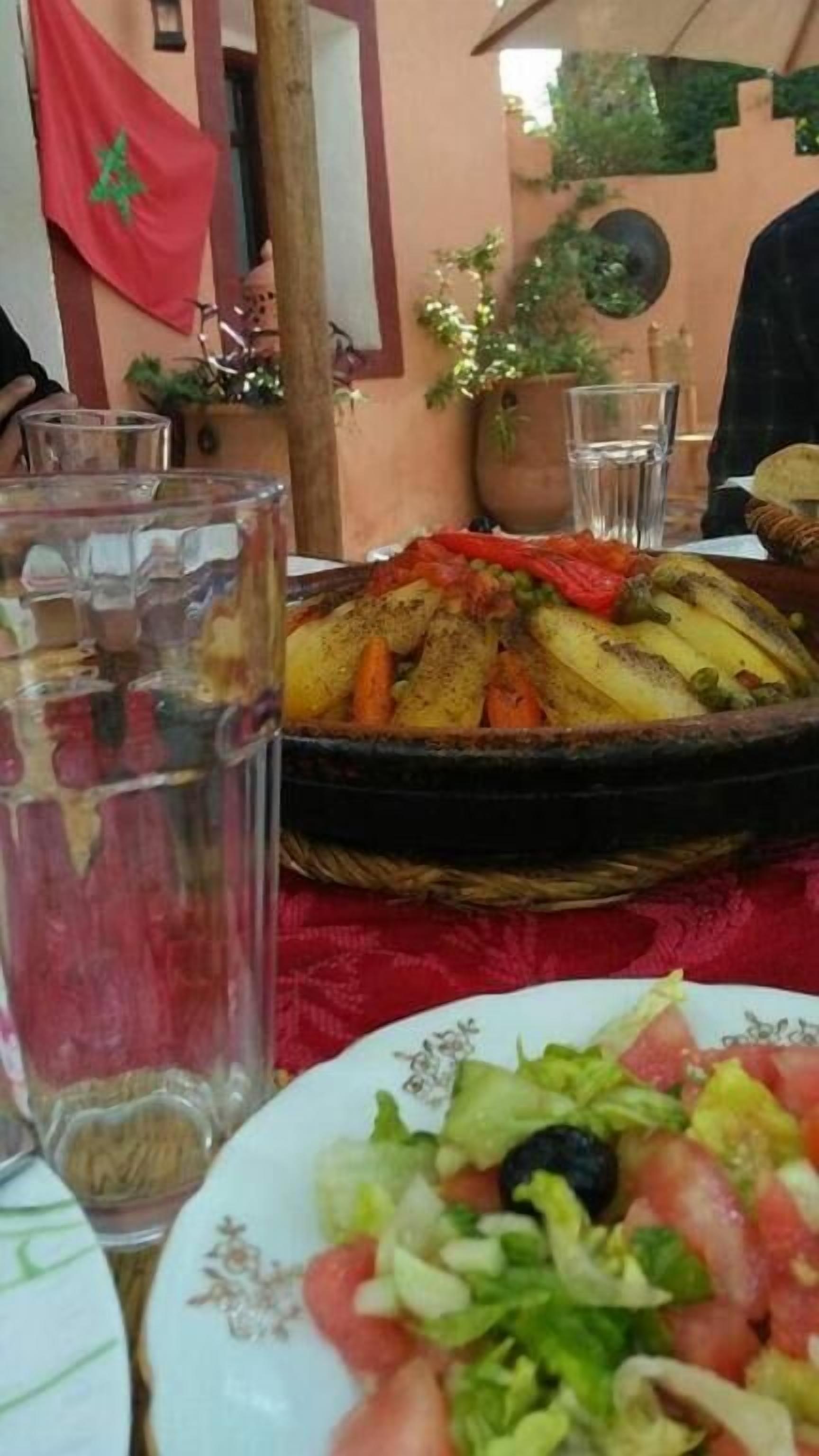 A dining table with a plate of salad, a basket of roasted vegetables, and a glass of water.