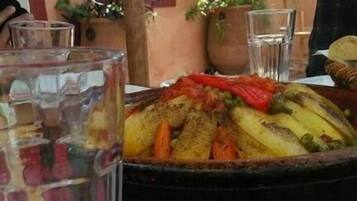 A dining table with a plate of salad, a basket of roasted vegetables, and a glass of water.