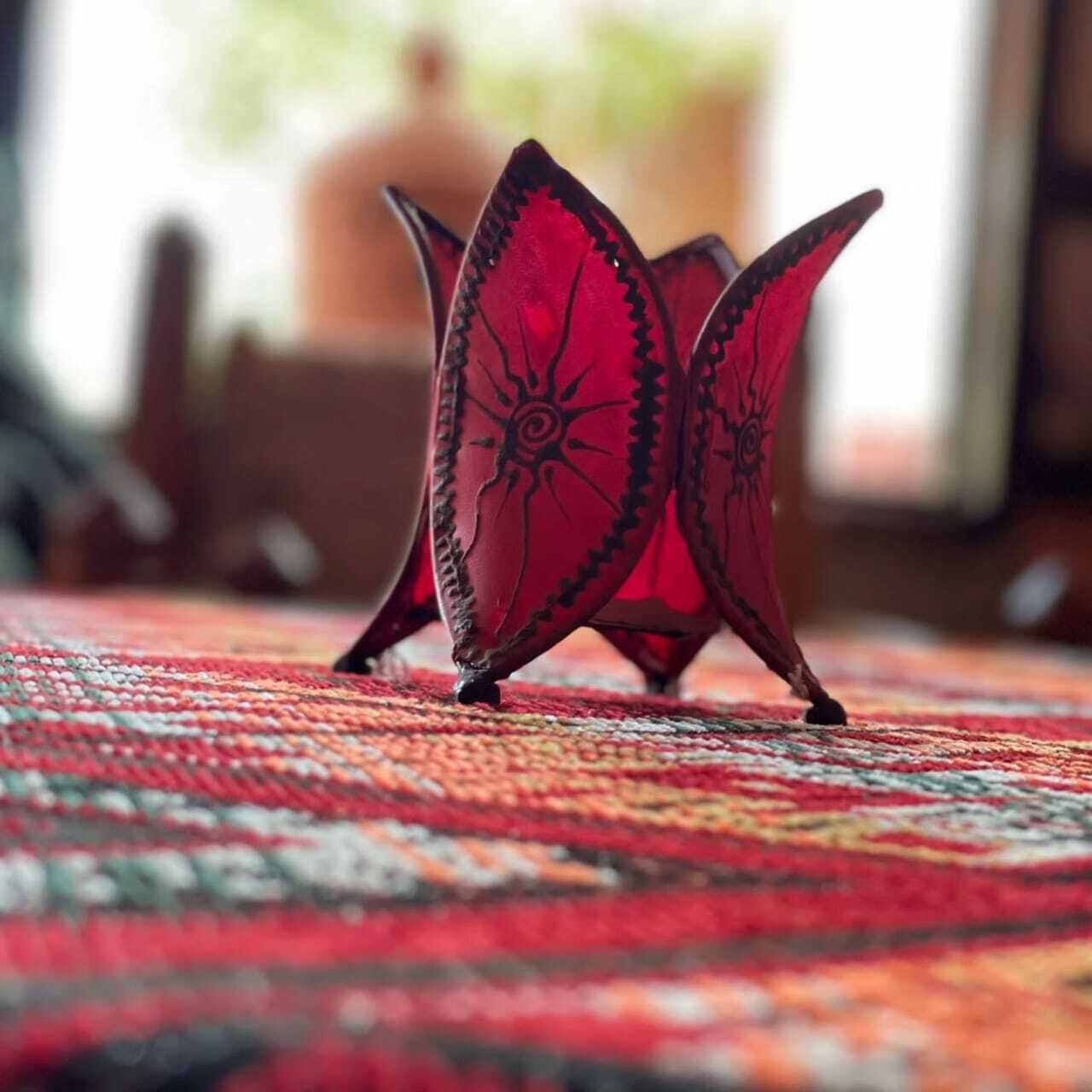Een rode decoratieve object met zwarte patronen op een getextureerd tapijt.