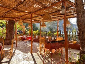 An outdoor patio with a thatched roof, wooden furniture, and potted plants. - Auberge le mouflon ouirgane (Ouirgane)
