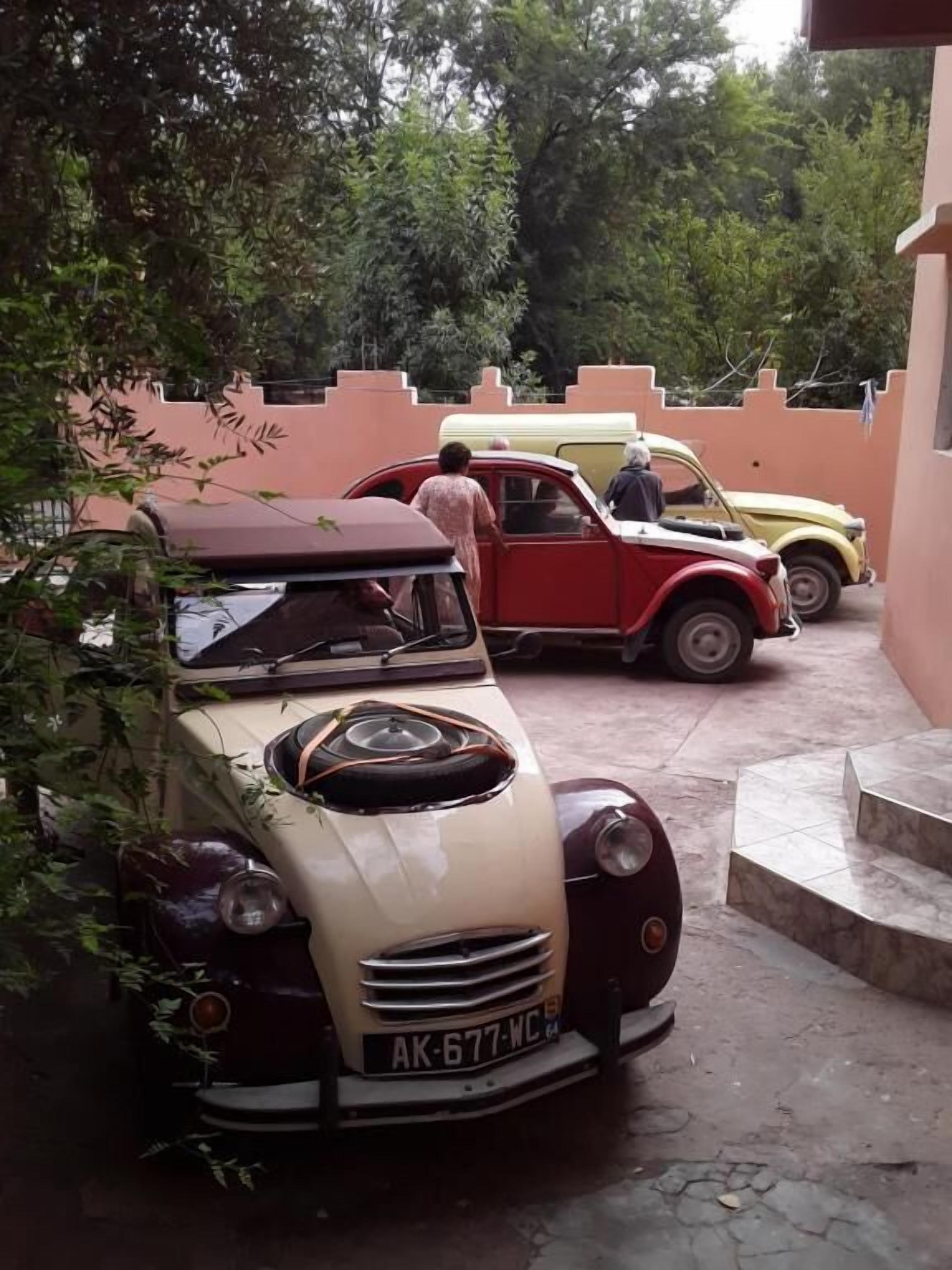 A vintage car parked in a driveway with a beige and red color scheme, a yellow car in the background, and a person standing near the beige car.