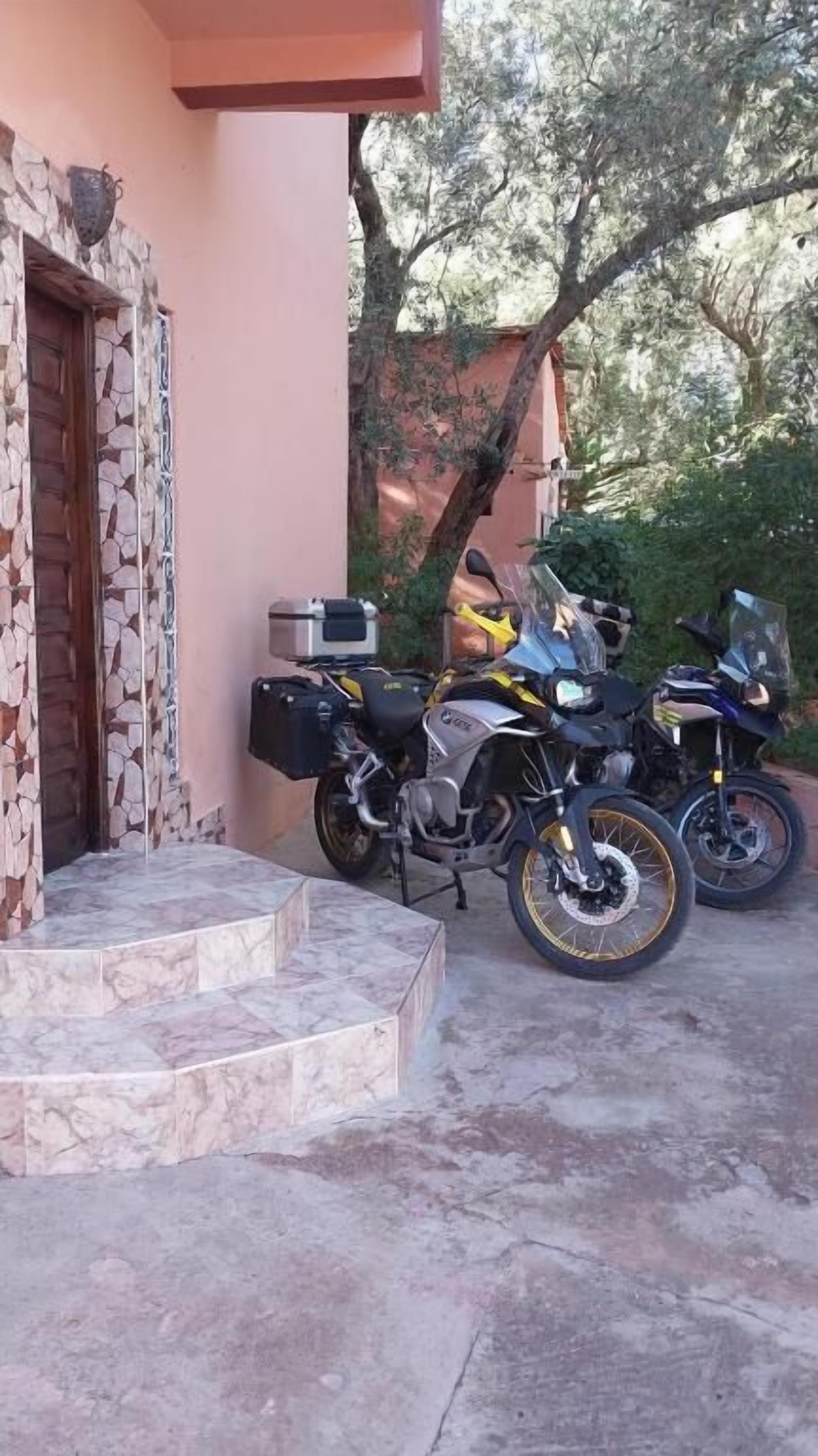 Un edificio con facciata in pietra e una scalinata che conduce a una porta. Due motociclette sono parcheggiate davanti.
