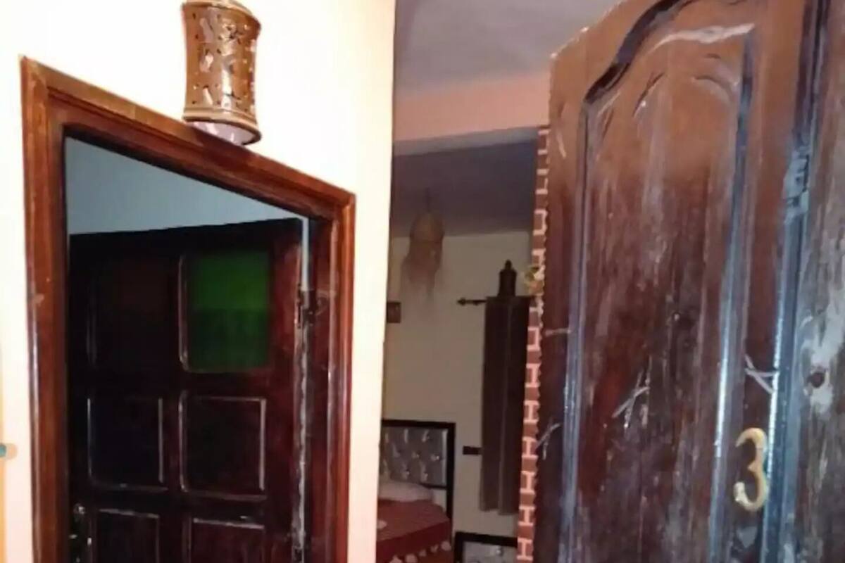 Une pièce avec une porte en bois, un lit recouvert d’une couvre-lit à motifs et un sol carrelé.