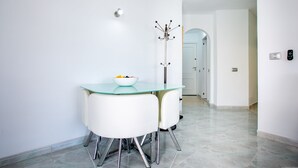 A modern dining area with a glass table, white chairs, and a bowl of fruit.
