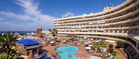 A resort with a large pool, multiple balconies, and a view of the ocean.