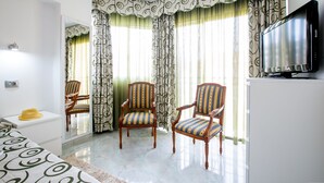 A hotel room with two wooden chairs with striped upholstery, a bed with a patterned bedspread, a television on a cabinet, and a large mirror on the wall.