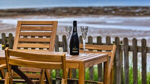 A wooden table with a bottle of wine and two glasses on it, overlooking a beach.