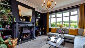 A living room with a fireplace, a sofa, a coffee table, and a large window with a view of greenery.