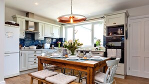 A modern kitchen with white cabinets, a wooden dining table set for four, and a large window providing natural light.