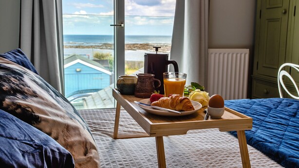 A breakfast tray on a bed with a view of the sea.