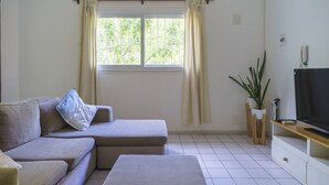 Una sala de estar con sofá, reposapiés, televisor y una ventana con cortinas.