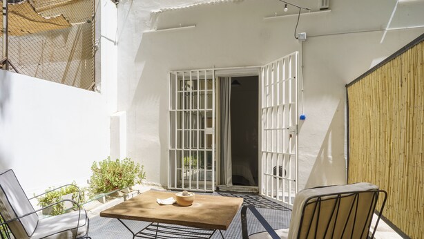 Un patio con una mesa y sillas, una valla de madera y una pared blanca.