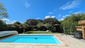 A rectangular swimming pool with a tiled deck, surrounded by a well-maintained lawn and trees. - Spacieuse Villa Avec Piscine et Climatisation (Aujargues)