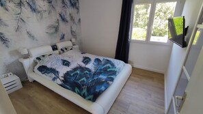 Um quarto com cama, mesa de cabeceira, janela e televisão.