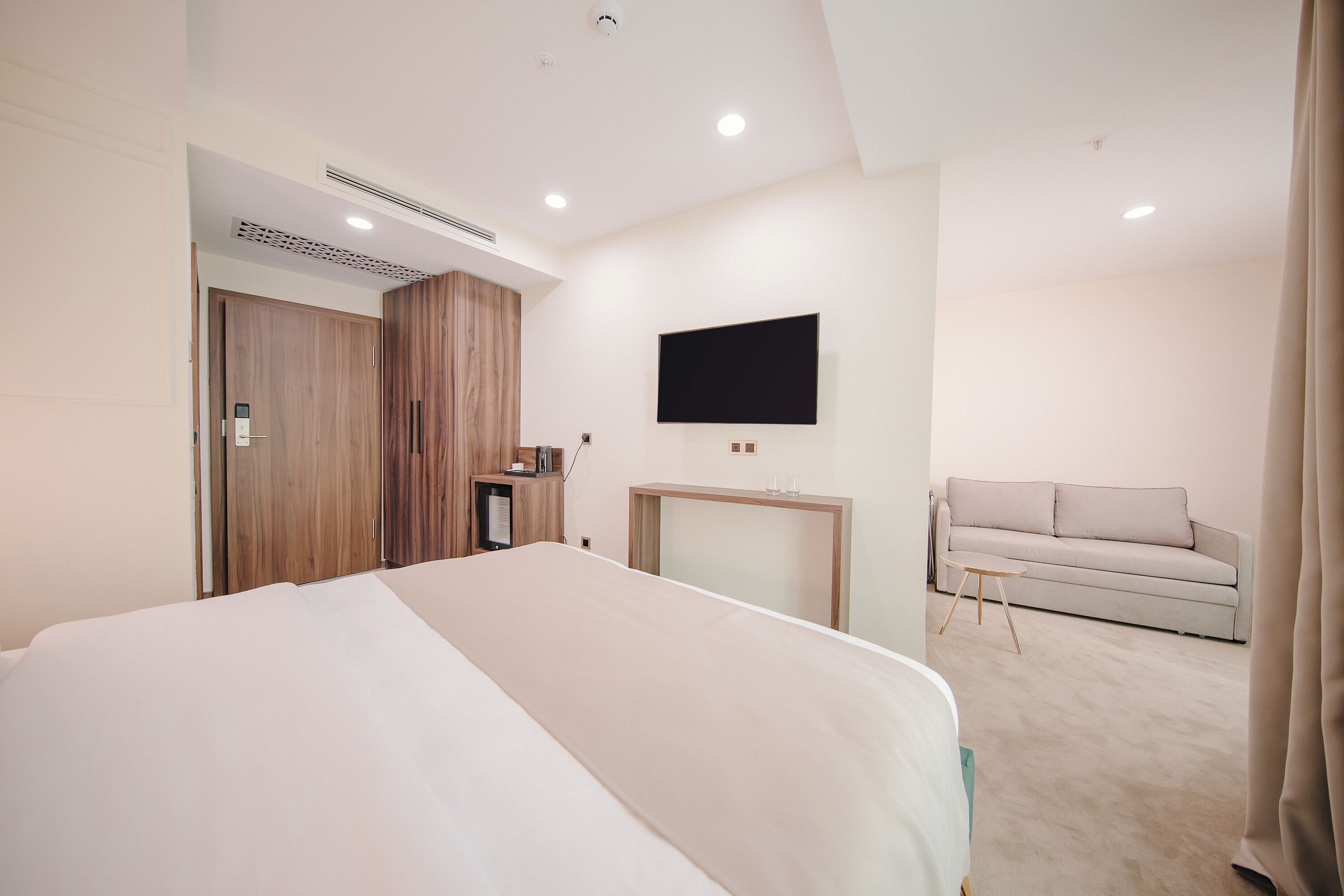 Una habitación de hotel moderna con una cama grande, un televisor montado en la pared, un sofá y un escritorio con una silla.