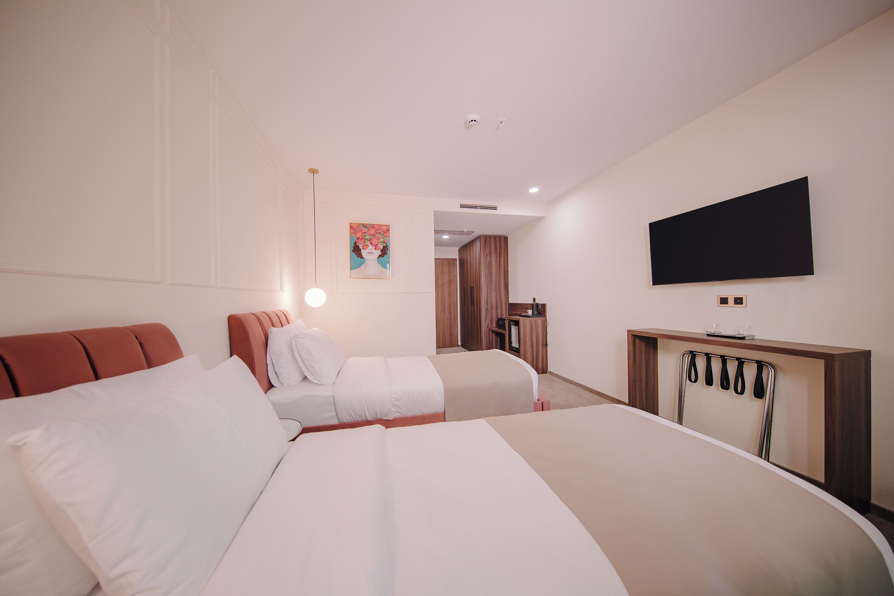 Habitación de hotel con dos camas, un televisor montado en la pared y un escritorio con espejo.