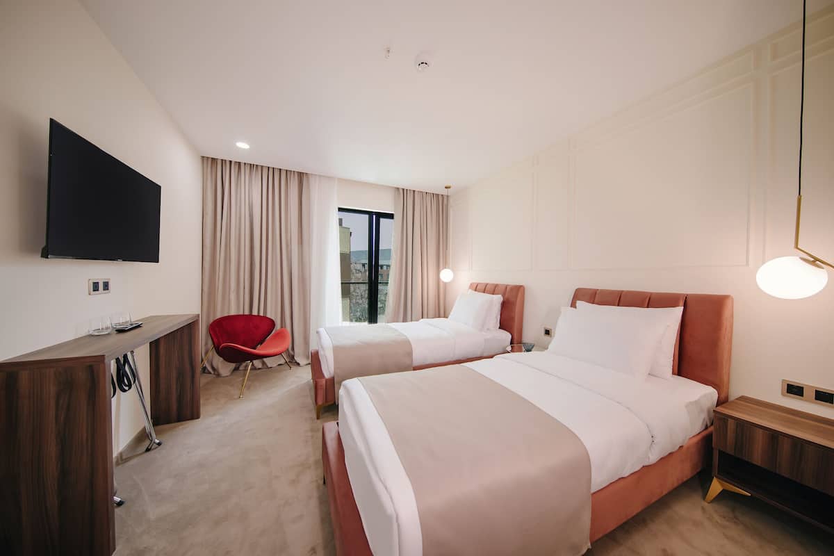 A hotel room with two beds, a desk, a TV, and a red chair.