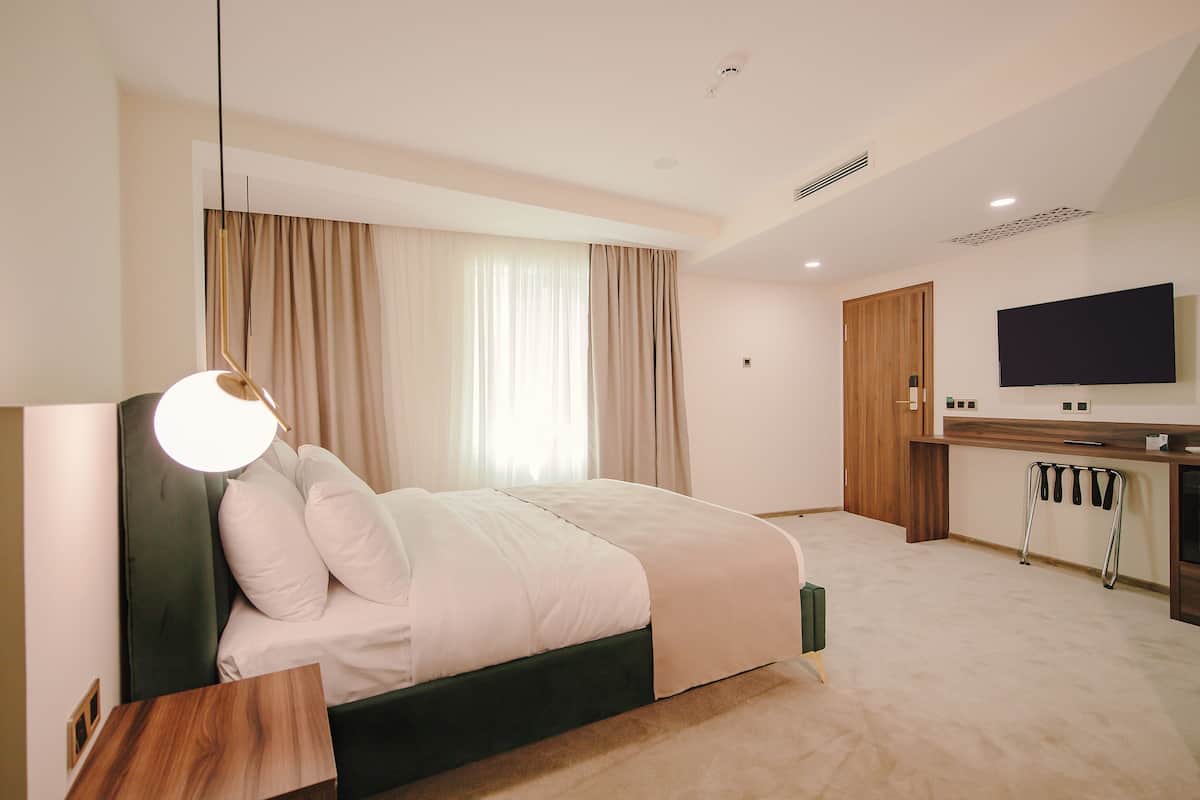 A modern hotel room with a bed, a desk, a television, and a large window with curtains.
