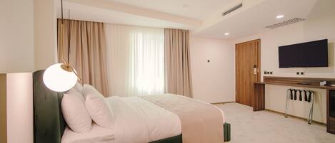 A modern hotel room with a bed, a desk, a television, and a large window with curtains.