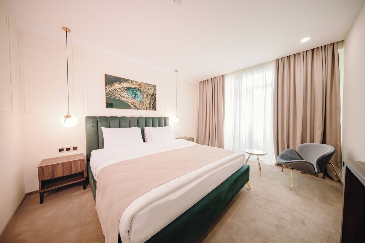 A hotel room with a large bed, a nightstand, a chair, and a painting on the wall.