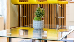 Een moderne keuken met een glazen tafel, een potplant en gele keukenkasten.