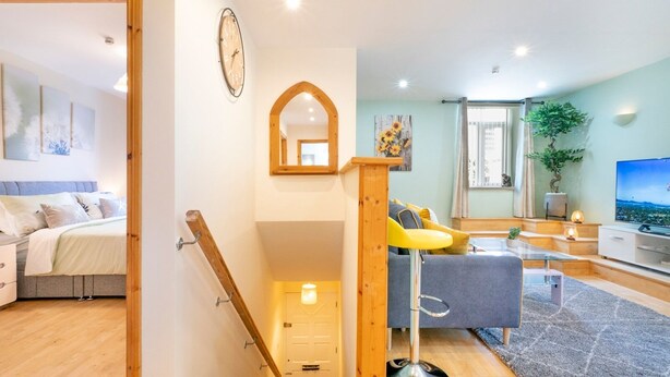 Een modern appartement met een trap, een woonkamer met een bank en televisie, en een slaapkamer met een bed en nachtkastjes.