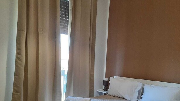 A hotel room with a bed, bedside table, lamp, air conditioning unit, and a view of the outdoors through the window. - Via Salvatore Meccio (Palermo)