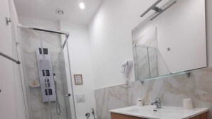A modern bathroom with a glass-enclosed shower, a wooden vanity with a mirror, and a marble floor. - Via Salvatore Meccio (Palermo)