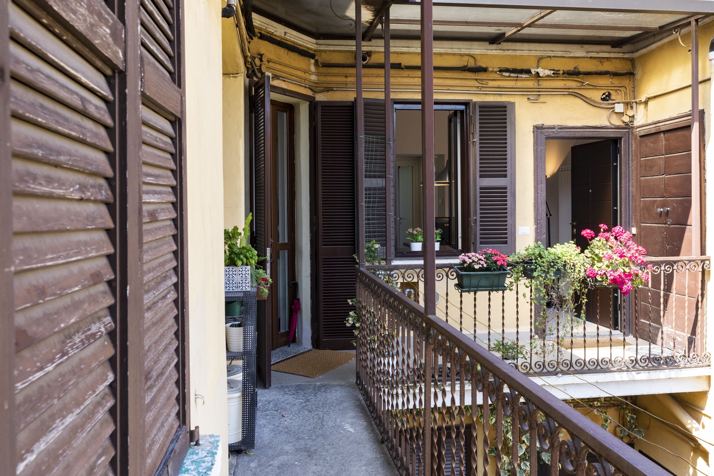 A balcony with a wrought iron railing, potted plants, and a door leading to an interior space.