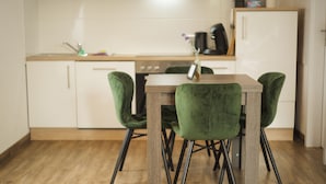 Een keuken met een houten tafel en groene stoelen, witte kasten en een houten vloer.