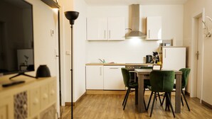 Een compacte keuken met witte kasten, een eettafel met stoelen en een moderne hanglamp.