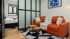 A modern hotel room with a bed, orange sofa, and a small wooden table. - Vibrant Central Studio at The Carrington (Cape Town)