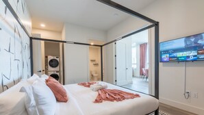 A modern hotel room with a large bed, a television mounted on the wall, and a view into the bathroom.
