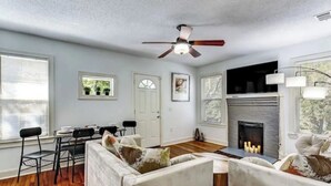 A living room with a fireplace, a ceiling fan, and a dining area with a table and chairs. - Luxury Historic Charm 1 mile to Forsyth Park (Savannah)
