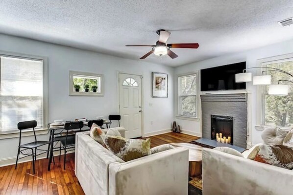 A living room with a fireplace, a ceiling fan, and a dining area with a table and chairs.