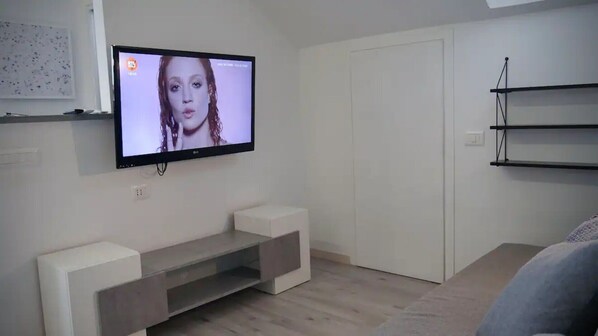 A modern living room with a flat-screen TV mounted on the wall, a minimalist entertainment unit, and a closed door.