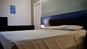 Una habitación de hotel con una cama, una mesita de noche, una lámpara de pared y una puerta.