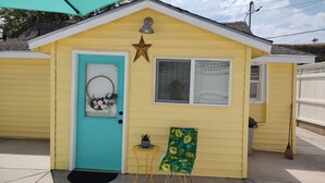 A small yellow building with a turquoise door, a star decoration above the door, and a window with a curtain.
