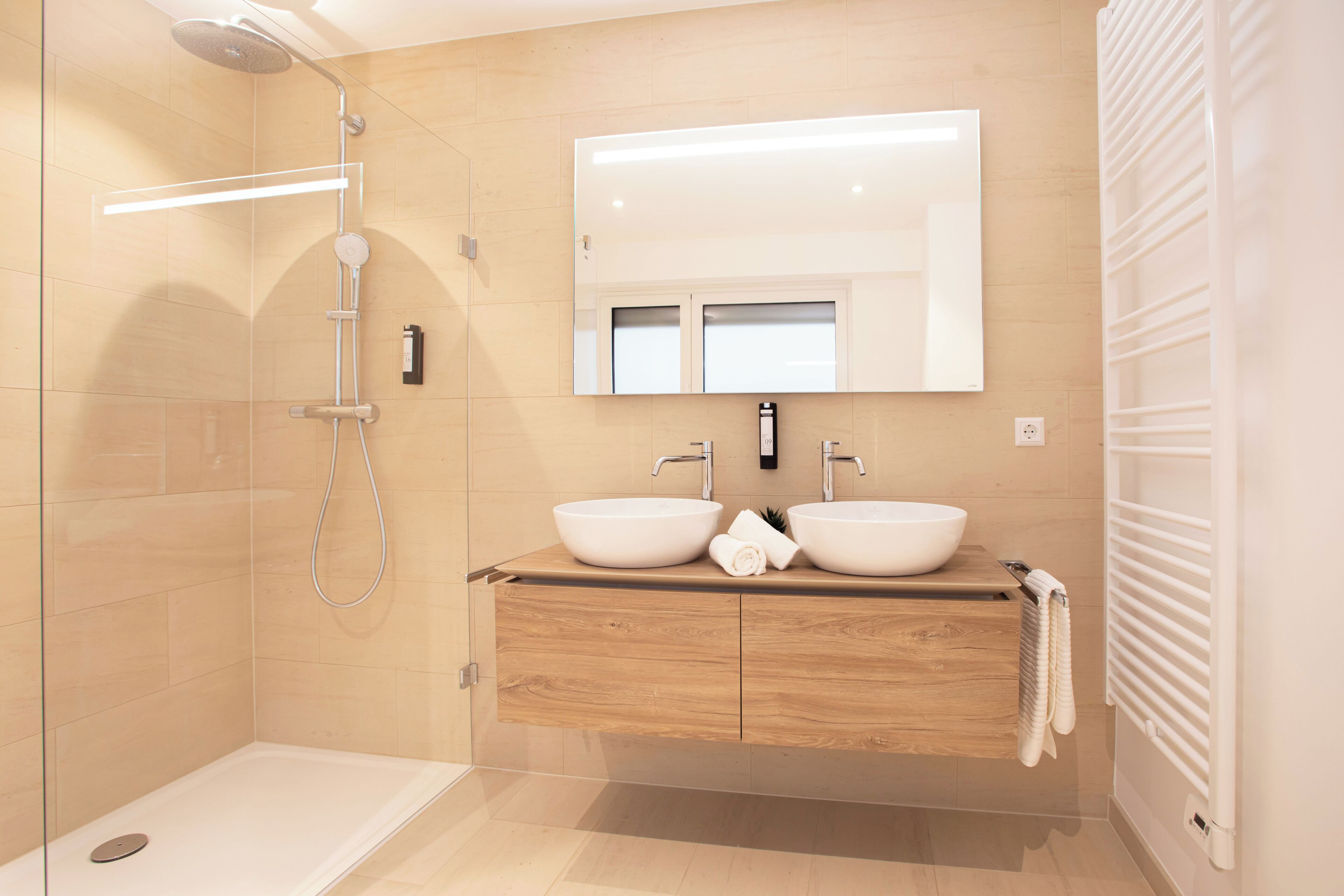 Un baño moderno con dos lavamanos, ducha a nivel y un espejo grande.