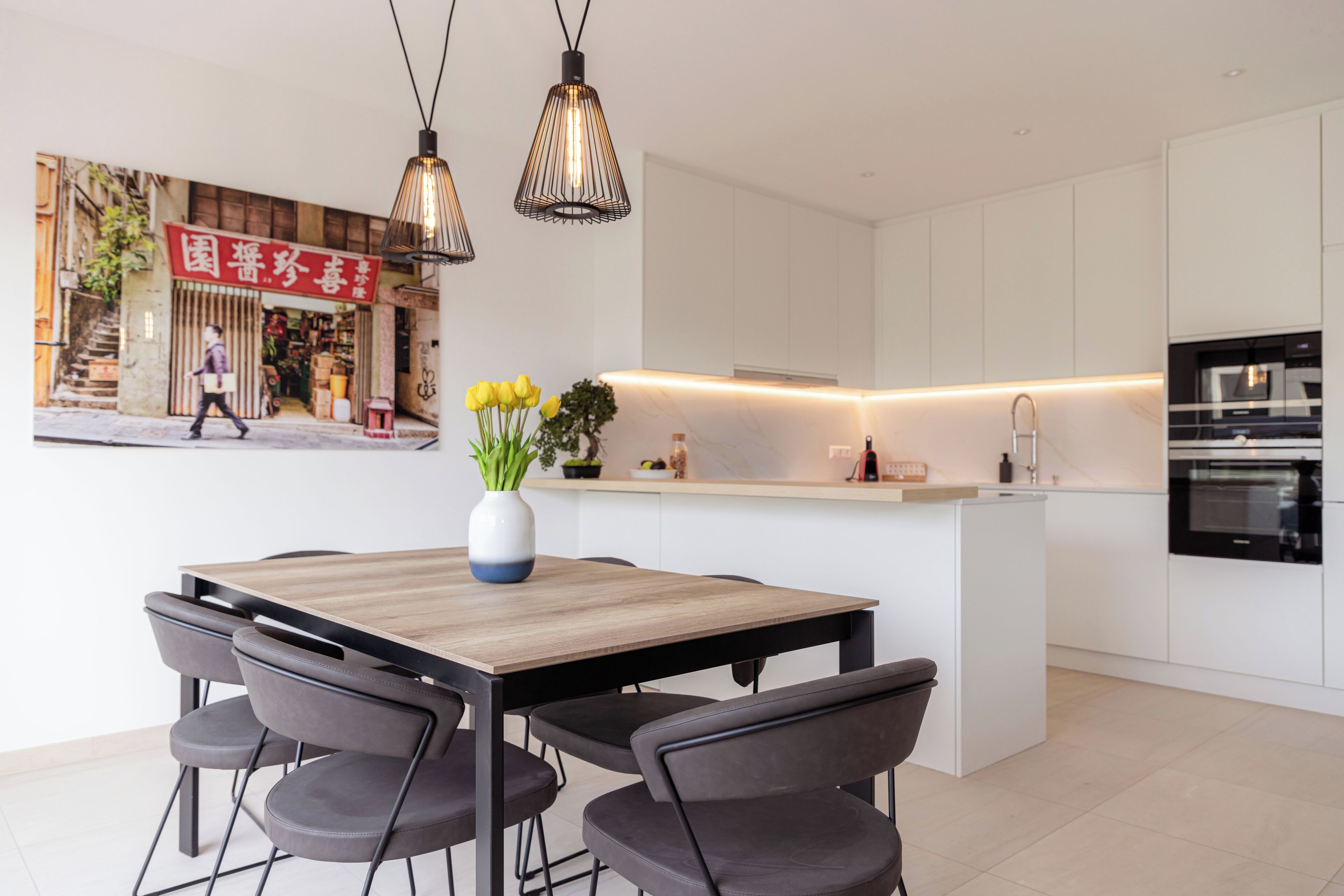 A modern kitchen with white cabinets, a wooden dining table, and pendant lighting.