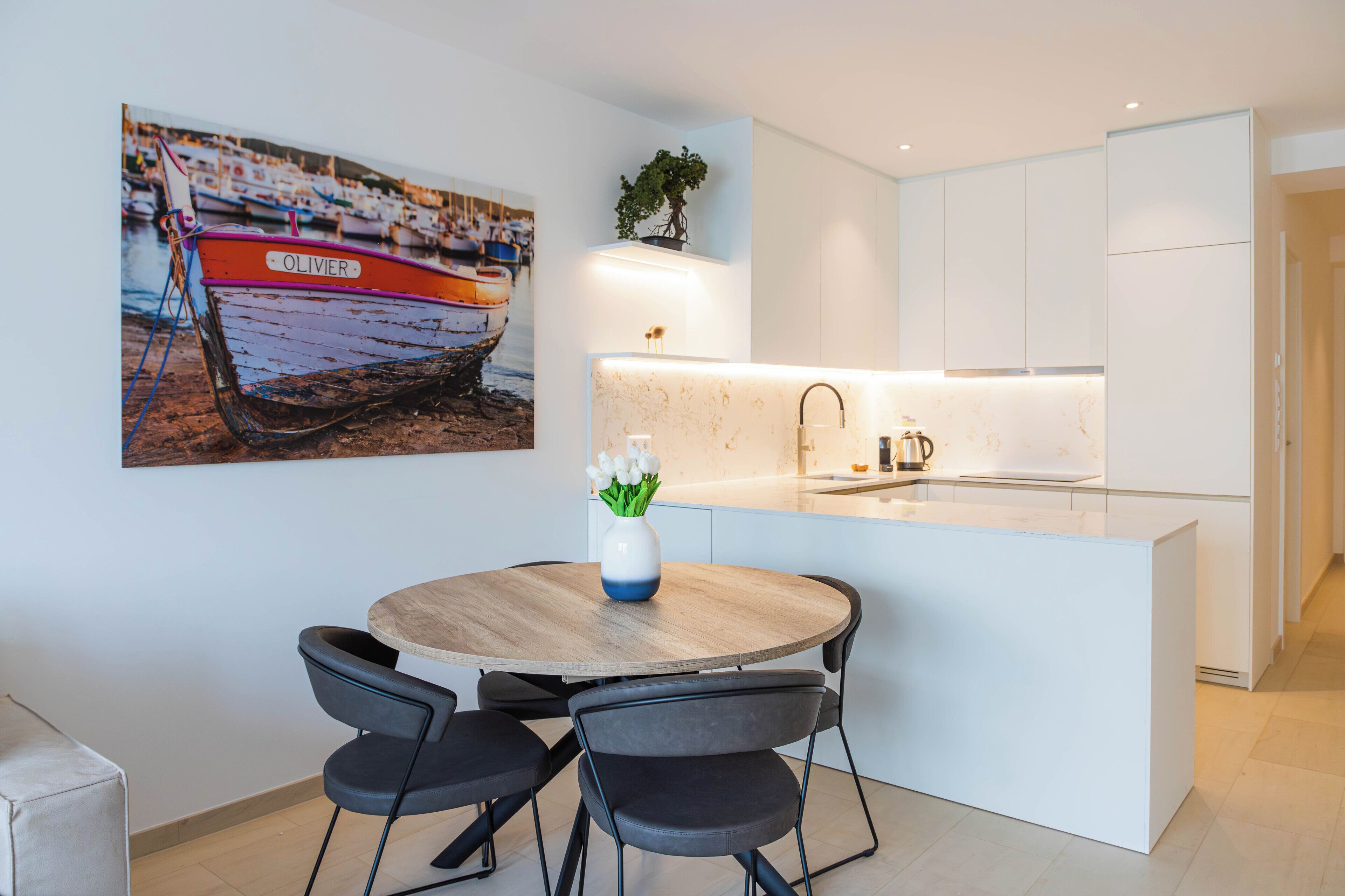A modern kitchen with white cabinets, a round wooden table, and two black chairs.