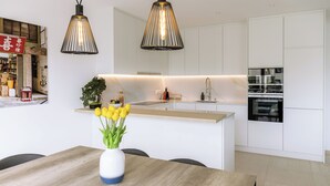 Une cuisine moderne avec des armoires blanches, un plan de travail en bois et un four encastré. Un vase rempli de fleurs jaunes est posé sur la table à manger.