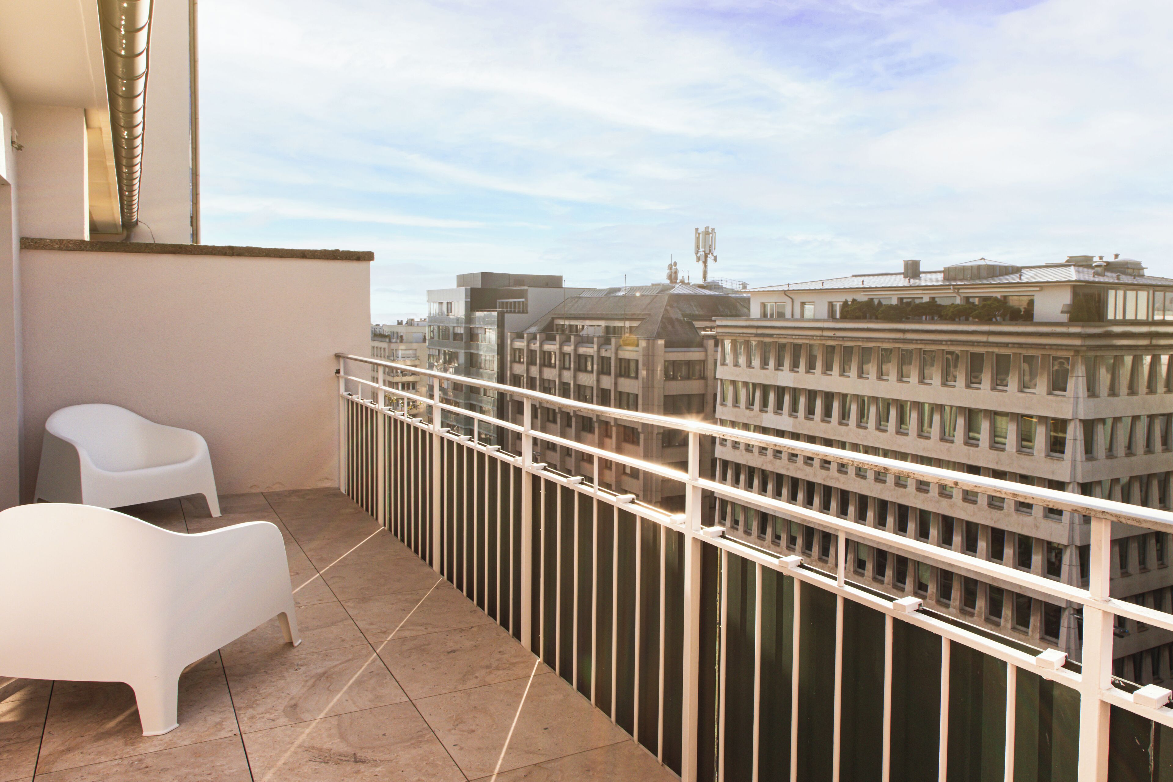 A balcony with white chairs and a view of city buildings.