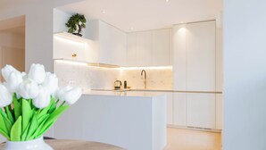 Une cuisine moderne avec des meubles blancs, un îlot central et une petite plante en pot placée sur l’étagère supérieure.