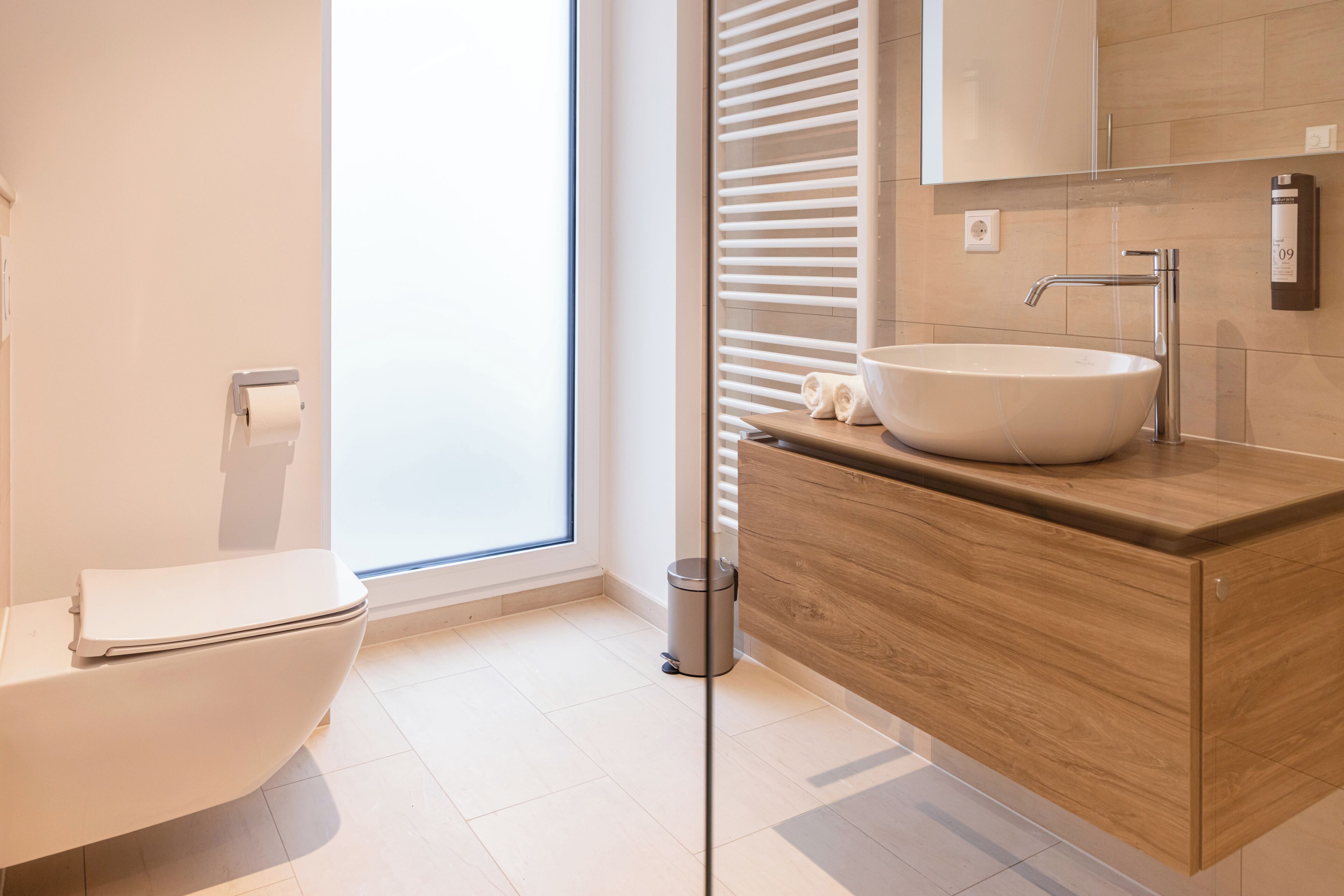 A modern bathroom with a white toilet, a wooden vanity with a sink, and a large mirror.