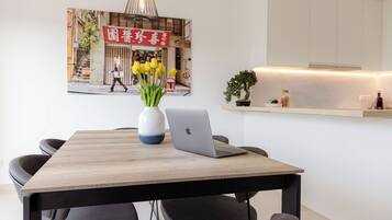 Uma zona de refeições moderna com uma mesa de madeira, cadeiras pretas, um laptop e um vaso de flores amarelas.