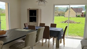 Zona pranzo con tavolo e sedie, una lampada a sospensione e vista su un paesaggio verde attraverso una porta in vetro.